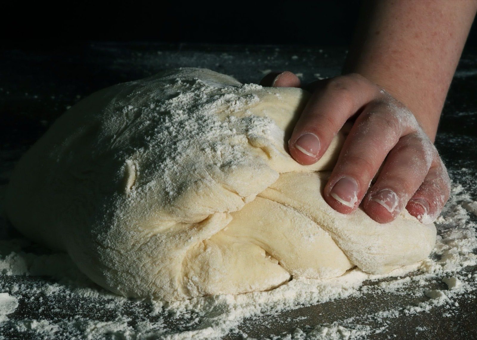 A baker's hand kneading dough on a table